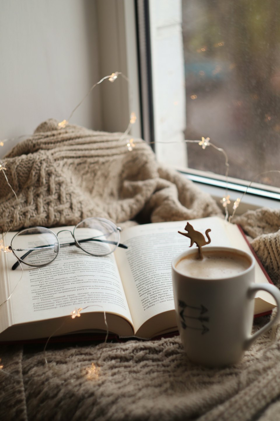 Reading glasses on an open book with coffee and fairy lights.