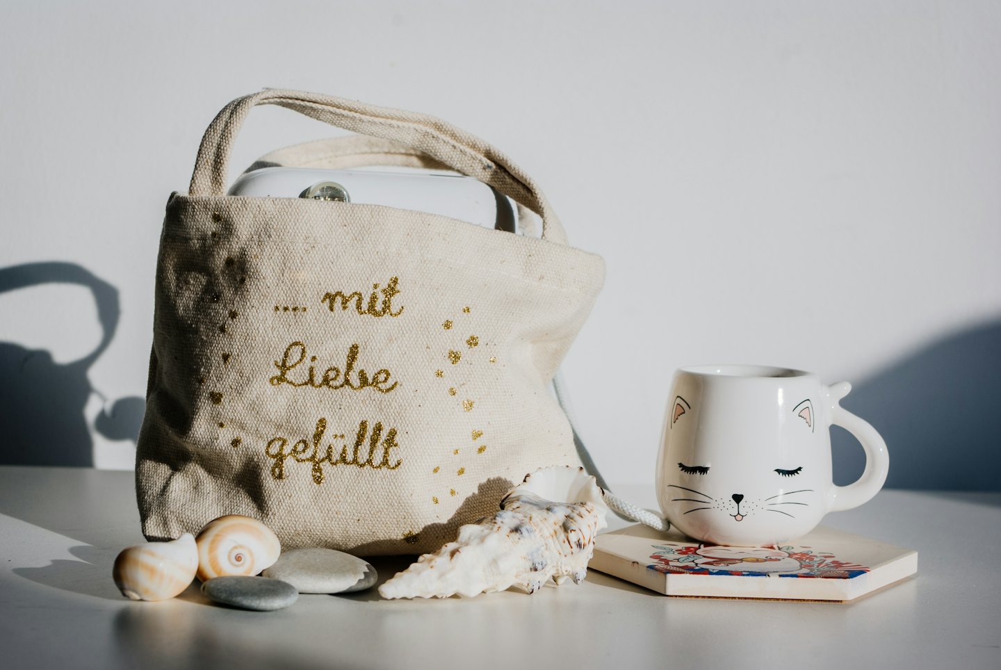 Beige tote bag with glitter text and cat mug by seashells.