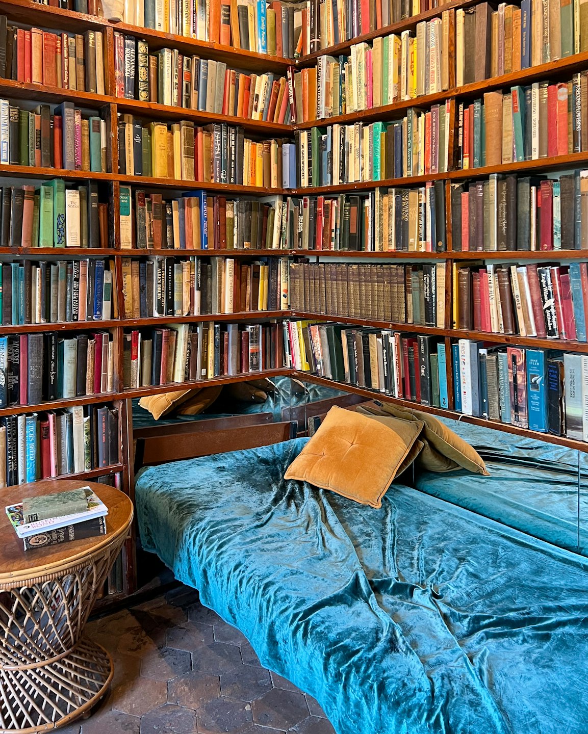 Cozy reading nook with teal bed and wooden bookshelves.
