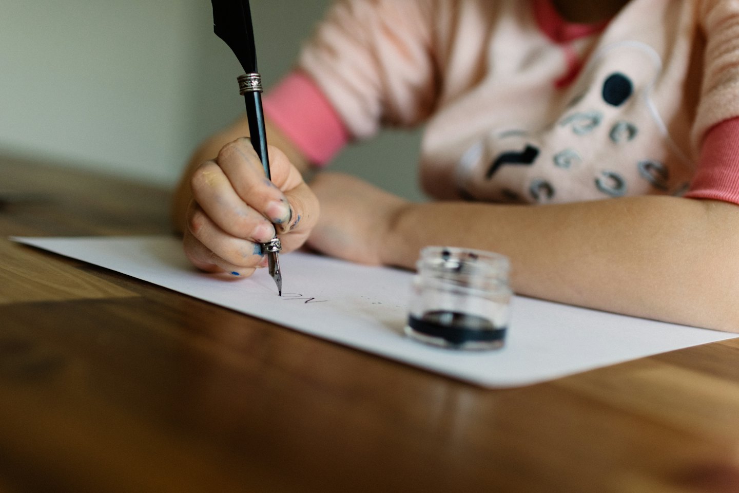 Hands holding a quill pen writing on paper on a wooden table.